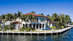 Elegant waterfront mansion in Fort Lauderdale, surrounded by palm trees and bright skies.